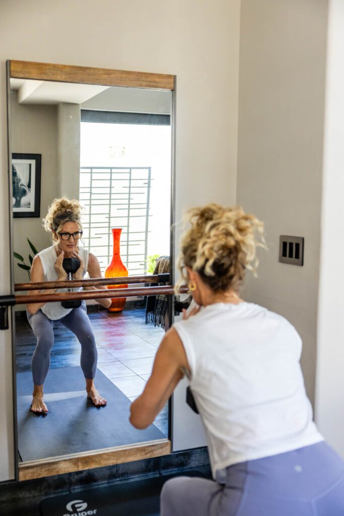woman working out with weights in front of mirror in home gym and embracing holistic health and wellness